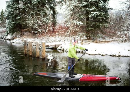 Ein Paddelboarder paddelt während eines Schneesturms einen kanadischen Fluss hinauf. Whistler, BC, Kanada. Stockfoto