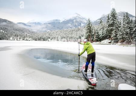 Ein Paddelboarder paddelt während eines Schneesturms einen kanadischen Fluss hinauf. Whistler, BC, Kanada. Stockfoto