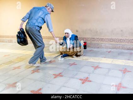 Ein Mann, der einer weiblichen Zigeunerbettlerin eine Änderung in einer Straße in Almaty, Kasachstan, gab Stockfoto