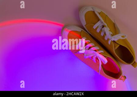 Trendige Mode weiße Sneakers auf Geometrie Podium auf abstrakt hellen Hintergrund. Neonlichter auf Freizeitschuhen. Violettes und orangefarbenes Gradientenlicht. Stockfoto