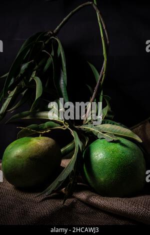 Mangofrucht mit Stielen und Blättern noch befestigt, Foto in dunkler Stimmung Stockfoto