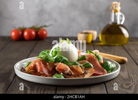 Selektiver Fokus auf italienischen Prosciutto mit Burrata-Käse, frischem Basilikum, Tomaten und Olivenöl. Geringe Schärfentiefe. Stockfoto