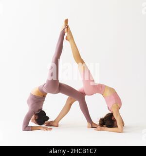 Zwei Frauen, die Yoga praktizieren und die paarige Übung von Eka Pada Viparita Dandasana, die Pose eines invertierten Stabs, durchführen, trainieren im Studio auf einer Brigg Stockfoto