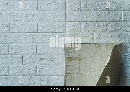 Die Tapete beginnt sich abzulösen. Die Tapete aus alten weißen Ziegeln schälte sich von der Wand im Raum, weil es feucht war oder sich nicht gut klebte. Reparieren Sie A Stockfoto
