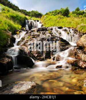 Natürlicher Blick auf den Wasserfall, der an einem sonnigen Tag stromabwärts fließt Stockfoto