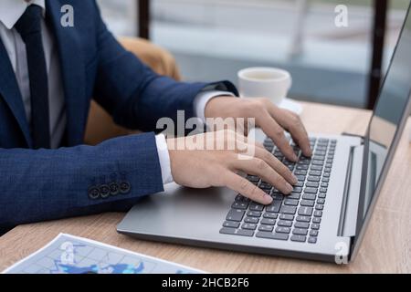 Hände eines jungen Wirtschaftswissenschaftlers oder Maklers berühren Tasten des Laptop-Tastenfelds, während sie am Tisch im Büro oder Café sitzen Stockfoto