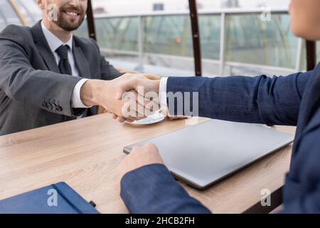 Zwei junge erfolgreiche Geschäftspartner in formalwear Handshaking über Tisch nach Verhandlungen und Abschluss Stockfoto
