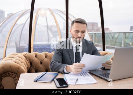Junge ernsthafte Ökonom in formalwear durch Papiere und Networking suchen, während sie am Tisch im Café sitzen Stockfoto