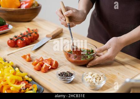Hände von Frauen, die hausgemachtes Ketchup mit Petersilienblättern in einer Glasschüssel mischen, während sie vegetarisches Essen in der Küche kochen Stockfoto