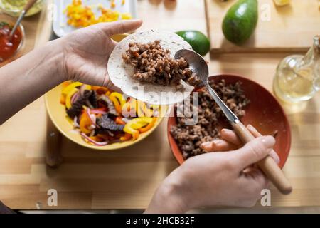 Hände einer jungen Frau mit Löffel, die gebratenes Hackfleisch auf Taco Tortillas legt, während sie nationale Gerichte kocht Stockfoto