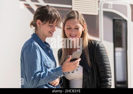 Zwei lächelnde Frauen checken ein Smartphone Stockfoto