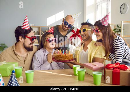 Happy Birthday Mädchen von ihren Freunden umgeben macht Wunsch sitzen vor Kuchen mit Kerzen. Stockfoto