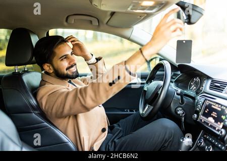 Befestigungsspiegel. Junger Geschäftsmann mit Brille, der den Rückspiegel fixiert, bevor er sein Auto fährt Stockfoto