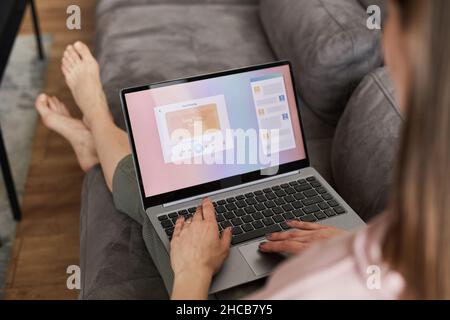 Rückansicht einer jungen Frau, die sich mit einem Laptop auf dem Sofa ausruht, online Videos ansieht oder online arbeitet Stockfoto