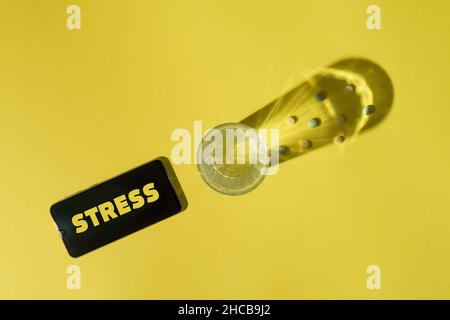 Pillen im Schatten von Glas Wasser und Smartphone mit Aufschrift Stress auf dem Bildschirm auf gelbem Hintergrund. Stress und Depression Konzept. Stockfoto