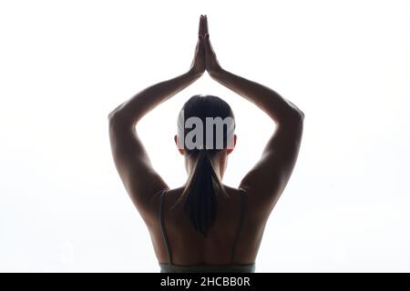 Rückansicht einer jungen Frau, die ihre Hände über ihren Kopf hielt und auf weißem Hintergrund Yoga machte Stockfoto