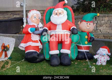 Die Familie Claus - Santa, Mrs. C, Junior und ihr Hund - bereiten sich auf den Urlaub vor, indem sie sich auf einer Wiese entspannen. In Whitestone, Queens, New York Stockfoto