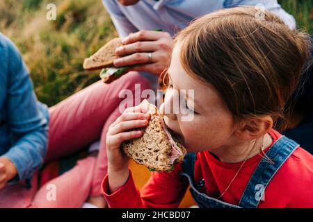 Mädchen essen Sandwich mit Eltern im Park Stockfoto