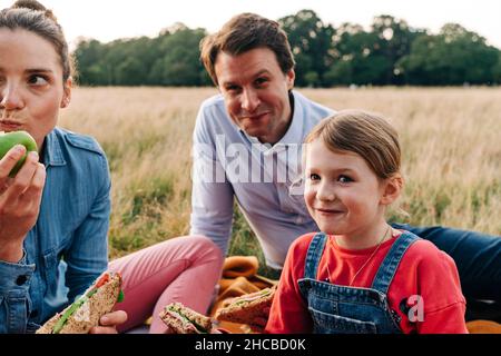 Lächelnde Tochter, die mit den Eltern im Park ein Sandwich gemacht hat Stockfoto