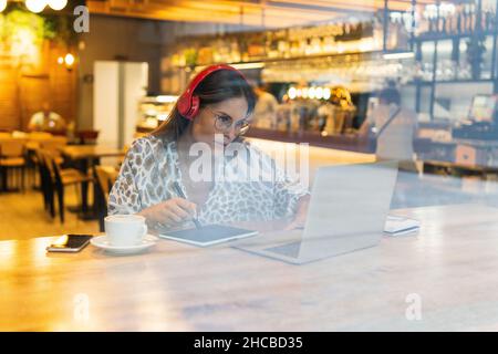 Junge Freiberuflerin, die im Café an Grafikkarten und Laptops arbeitet Stockfoto