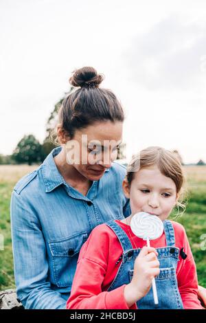 Mutter schaut auf die Tochter, die im Park Lollipop isst Stockfoto