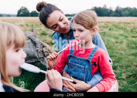 Frau, die im Park ein Mädchen beim Lutscher-Essen ansieht Stockfoto