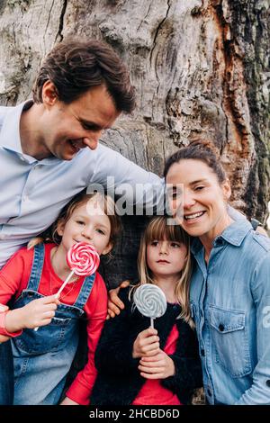 Lächelnde Eltern mit Töchtern, die im Park Lutscher essen Stockfoto