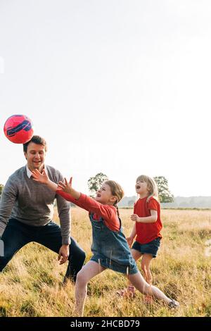 Glückliche Geschwister und Vater spielen mit Ball im Park Stockfoto