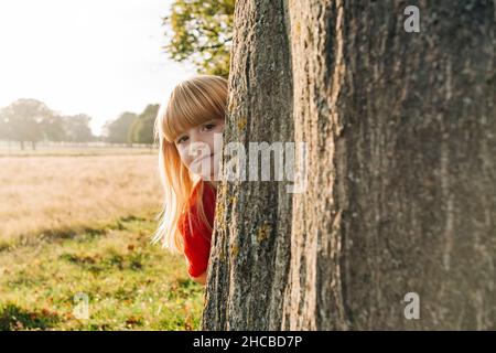 Mädchen versteckt sich hinter Baum im Park Stockfoto