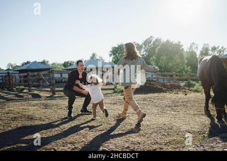 Mutter und Tochter laufen am sonnigen Tag auf dem Pferdehof auf den Vater zu Stockfoto