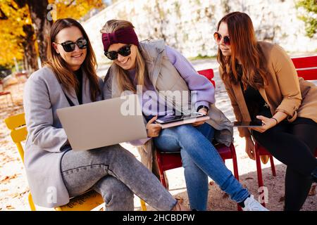 Lächelnde Geschäftsfrau, die im Herbstpark über einen Laptop mit Kollegen diskutiert Stockfoto