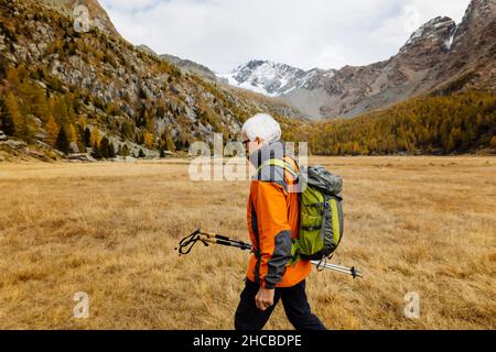 Senior Rucksacktourist mit Stöcken, die auf Gras wandern Stockfoto