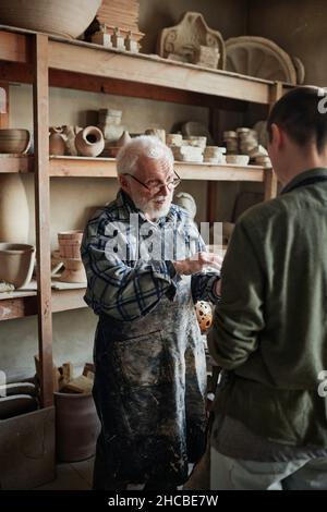 Senior Töpfer diskutiert die Arbeit mit seinem Assistenten, während sie Skulpturen im Studio machen Stockfoto