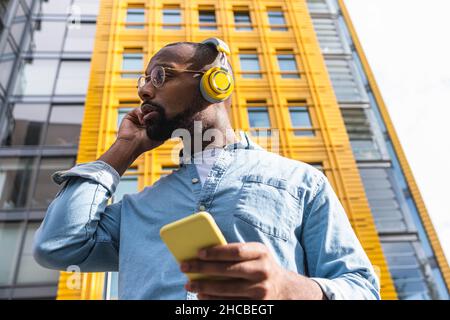 Mann hört Musik auf kabellosen Kopfhörern vor dem modernen Gebäude Stockfoto