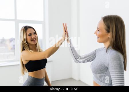 Lächelnde Fitness-Frauen heben die Hände, um eine hohe fünf während des Trainings zu geben. Fröhliche sportliche Frauen genießen das Fitnesstraining in einem Fitnessstudio. Stockfoto