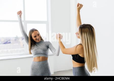 Lächelnde Fitness-Frauen heben die Hände, um eine hohe fünf während des Trainings zu geben. Fröhliche sportliche Frauen genießen das Fitnesstraining in einem Fitnessstudio. Stockfoto