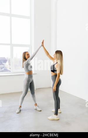 Lächelnde Fitness-Frauen heben die Hände, um eine hohe fünf während des Trainings zu geben. Fröhliche sportliche Frauen genießen das Fitnesstraining in einem Fitnessstudio. Stockfoto