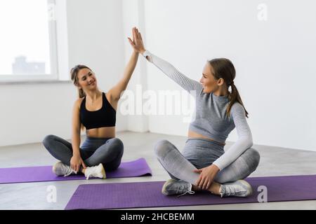 Lächelnde Fitness-Frauen heben die Hände, um eine hohe fünf während des Trainings zu geben. Fröhliche sportliche Frauen genießen das Fitnesstraining in einem Fitnessstudio. Stockfoto
