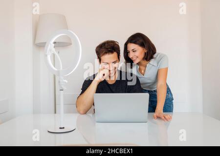 Glückliche junge Frau, die zu Hause einen freiberuflichen Mann ansieht, der am Laptop arbeitet Stockfoto