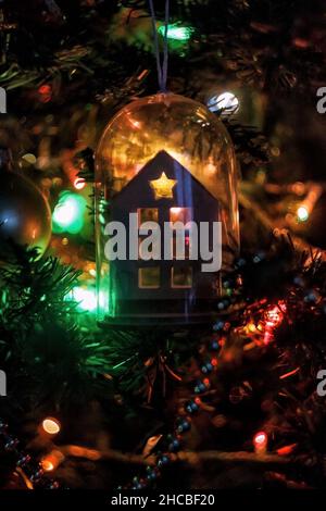 Ein Spielzeug in Form eines Hauses hängt an einem Weihnachtsbaum mit brennenden Lichtern. Silhouette Stockfoto