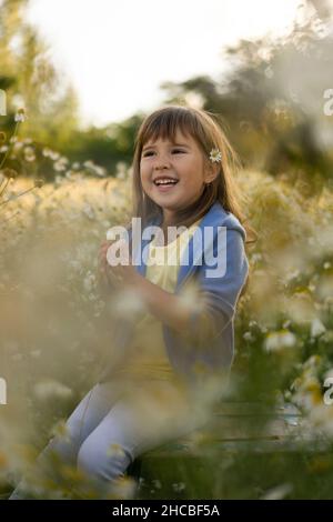Glückliches Mädchen in lässiger Kleidung, das inmitten von Pflanzen auf der Wiese sitzt Stockfoto