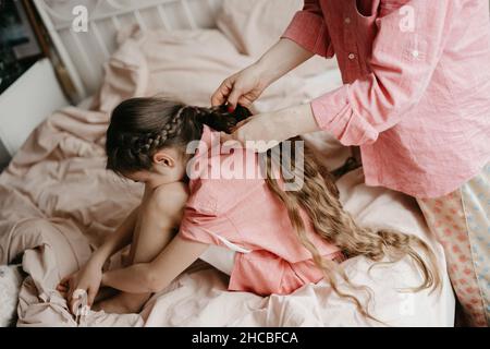 Mutter flechtet die Haare der Tochter zu Hause auf das Bett Stockfoto