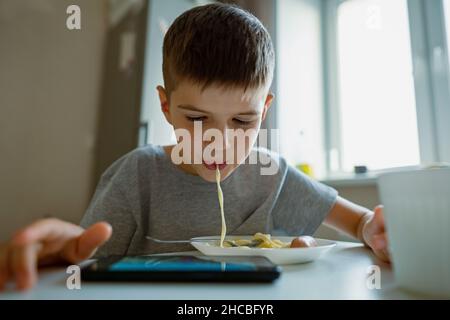 Junge, Kind isst Nudeln, die ihm lange Nudeln in den Mund saugen Stockfoto