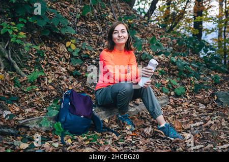 Lächelnder Wanderer mit Rucksack, der die Flasche auf dem Holzstock hält Stockfoto