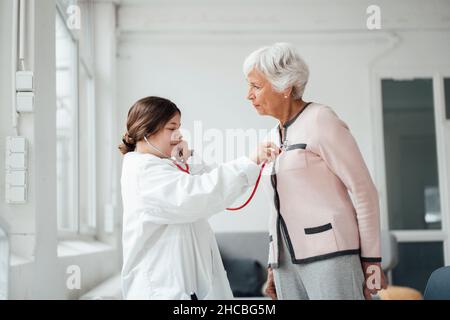 Enkelin mit Stethoskop überprüft Großmutter zu Hause Stockfoto