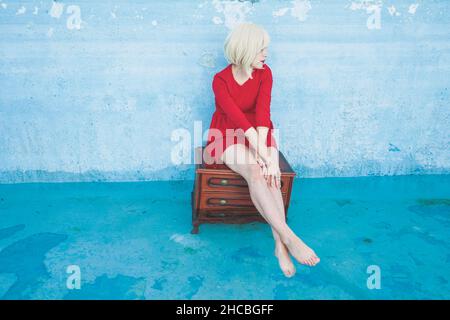 Frau, die auf einer Kommode aus Holz im blauen Swimmingpool sitzt Stockfoto