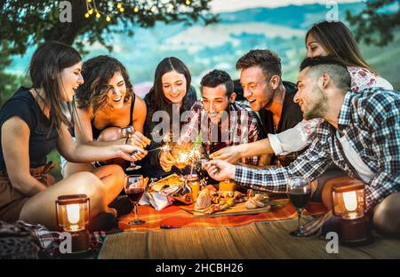 Glückliche Freunde, die Spaß mit dem Feuer haben funkelt - Junge Menschen Millennials campen beim Picknick nach Sonnenuntergang - Junge Menschen genießen Wein beim Sommergrillen Stockfoto