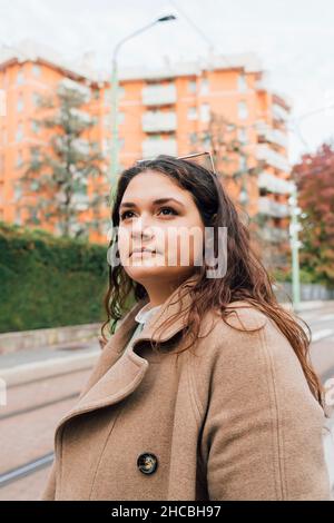 Kontemplative kurvige Frau in braunem Mantel Stockfoto