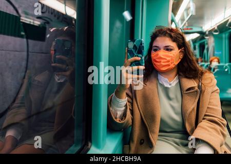 Junge Frau trägt eine schützende Gesichtsmaske mit einem Smartphone in der Seilbahn Stockfoto