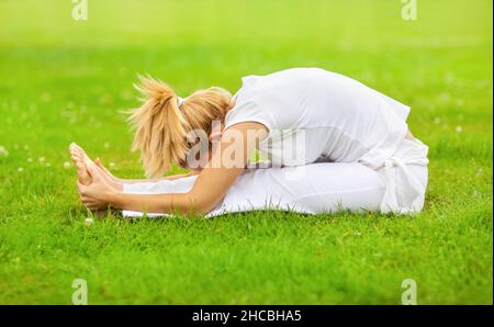 Flexible junge Frau, die im Park Yoga auf Gras trainiert Stockfoto